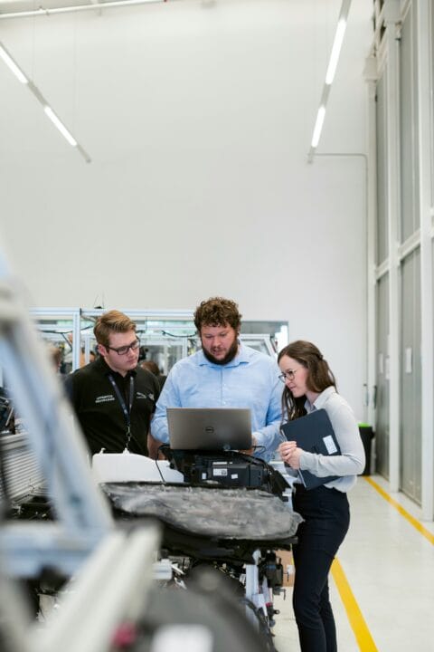 Zwei Kollegen (ein Mann, eine Frau) und ein Elektrotechniker besprechen gemeinsam Inhalte auf einem Laptop im Büro